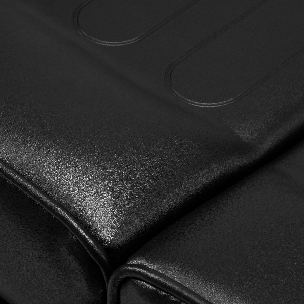 Close-up of black hydraulic treatment chair upholstery with stitched lines.